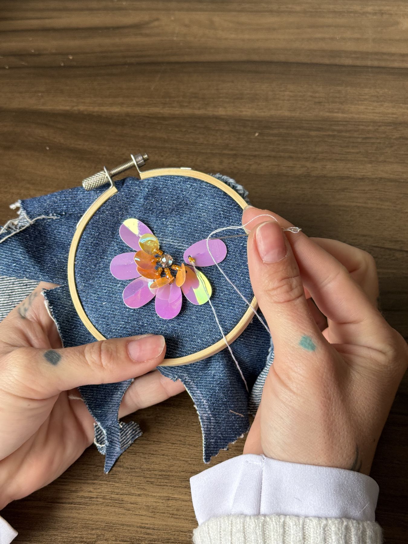 Las manos de Catterina bordando una flor de lentejuelas en el bastidor